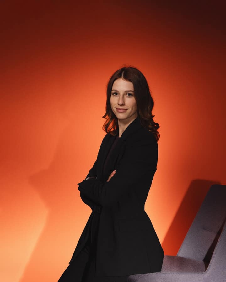 Alexandra Galler stehend vor einem orange-roten Hintergrund