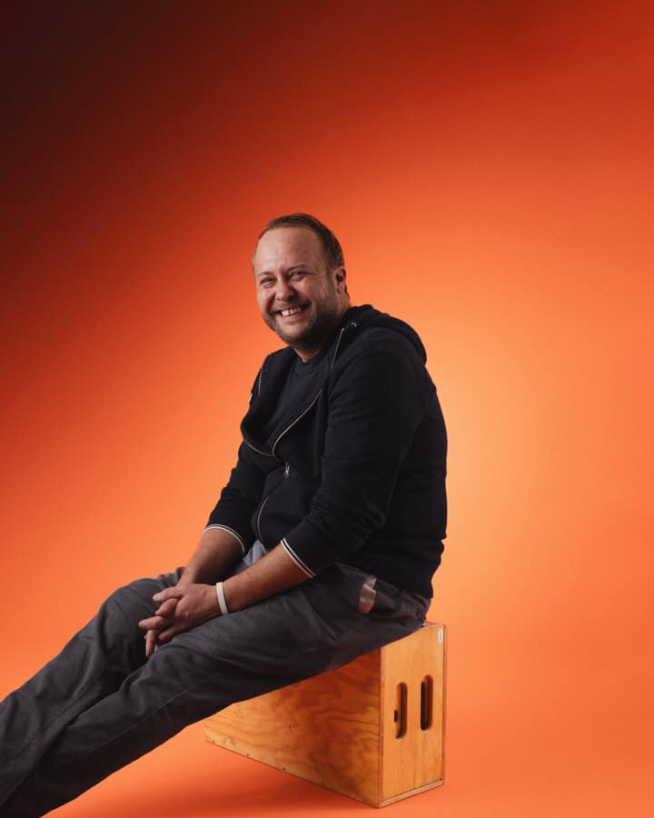 Gernot Hofbauer sitzend vor einem orange-roten Hintergrund